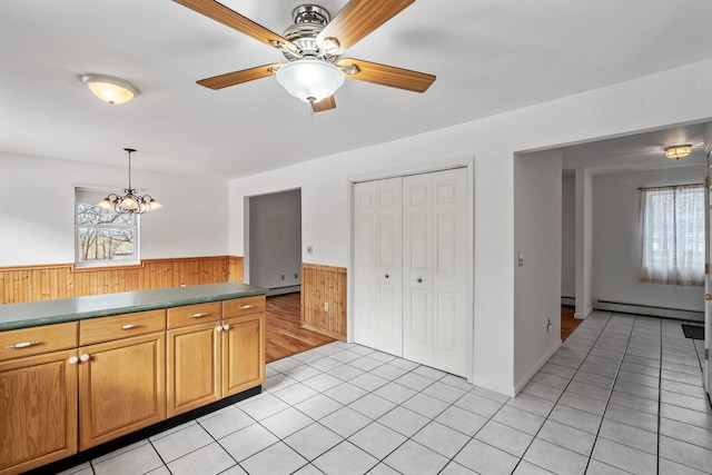 kitchen with light tile patterned floors, baseboard heating, hanging light fixtures, wooden walls, and ceiling fan with notable chandelier