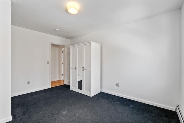 unfurnished bedroom with dark carpet, a closet, and a baseboard heating unit