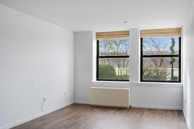 empty room featuring radiator, a healthy amount of sunlight, baseboards, and wood finished floors