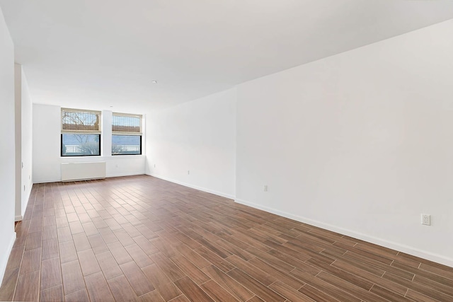 empty room with radiator, dark wood-type flooring, and baseboards