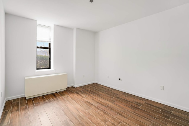 spare room with radiator, baseboards, and wood finished floors