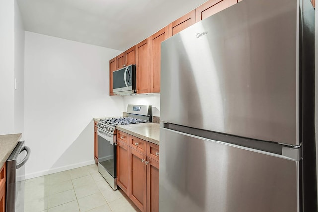 kitchen featuring light tile patterned floors, light countertops, appliances with stainless steel finishes, and brown cabinets