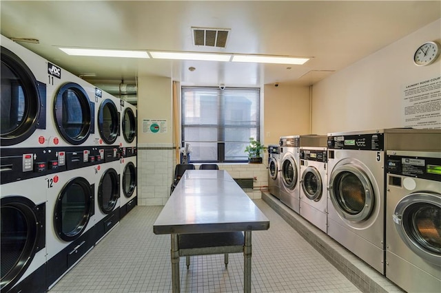 community laundry room featuring light tile patterned flooring, washing machine and dryer, stacked washer / dryer, visible vents, and tile walls