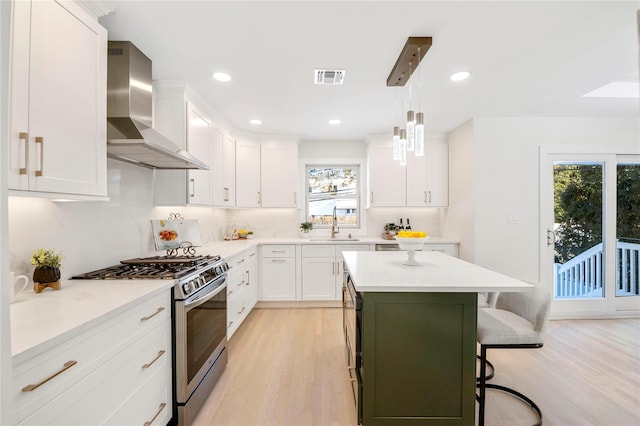 kitchen with decorative light fixtures, white cabinetry, wall chimney exhaust hood, and stainless steel range with gas cooktop