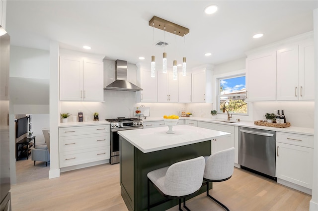 kitchen with white cabinets, pendant lighting, wall chimney range hood, and appliances with stainless steel finishes