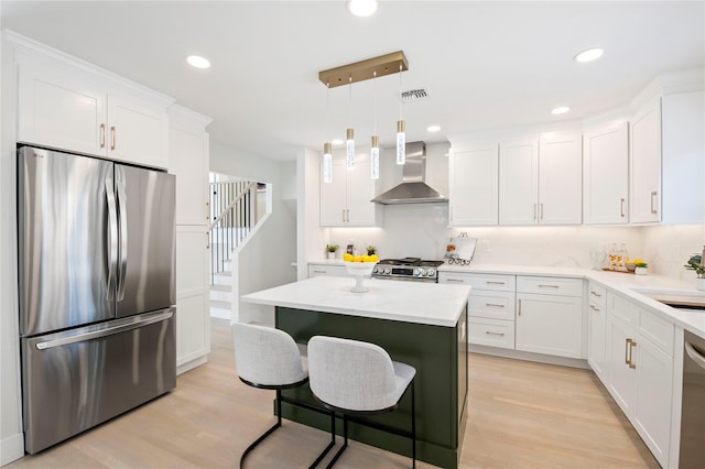 kitchen with a center island, appliances with stainless steel finishes, wall chimney range hood, light hardwood / wood-style flooring, and pendant lighting