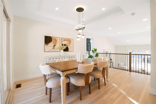 dining room featuring light hardwood / wood-style floors, a raised ceiling, and vaulted ceiling