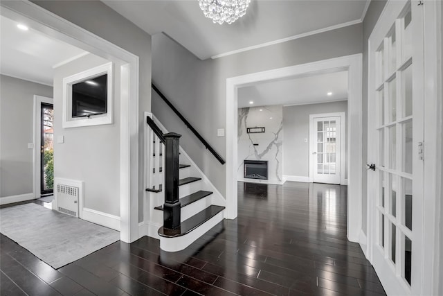 entryway featuring dark hardwood / wood-style floors, a high end fireplace, crown molding, and an inviting chandelier