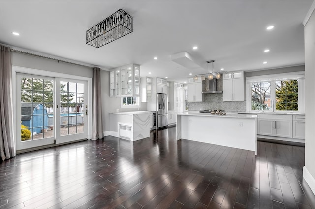 kitchen with stainless steel refrigerator with ice dispenser, decorative light fixtures, a kitchen island, wall chimney exhaust hood, and white cabinets