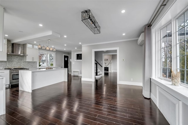 kitchen with high end stove, wall chimney range hood, white cabinets, an AC wall unit, and a center island