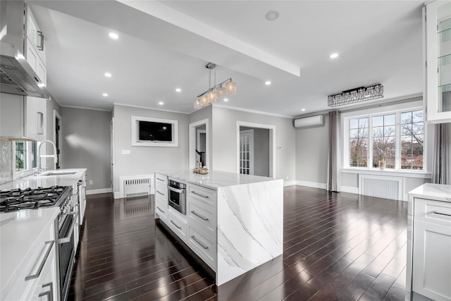 kitchen featuring radiator heating unit, wall chimney exhaust hood, decorative light fixtures, stainless steel range, and white cabinetry