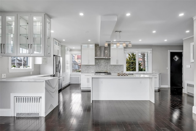 kitchen featuring wall chimney exhaust hood, stainless steel fridge, white cabinets, and radiator heating unit