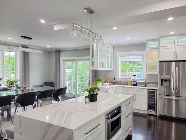 kitchen with white cabinets, beverage cooler, appliances with stainless steel finishes, decorative light fixtures, and light stone counters