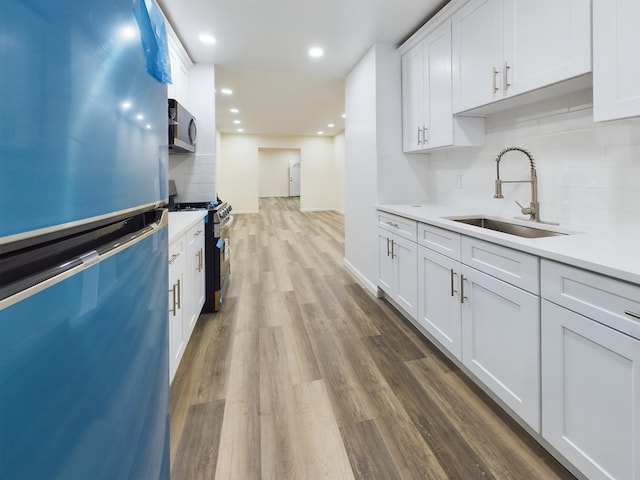 kitchen with stainless steel range with gas cooktop, light countertops, freestanding refrigerator, white cabinetry, and a sink