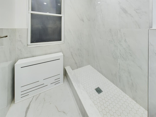 bathroom featuring marble finish floor, a tile shower, and tile walls