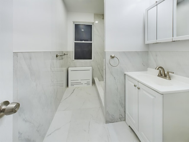 bathroom featuring a marble finish shower, heating unit, marble finish floor, vanity, and tile walls