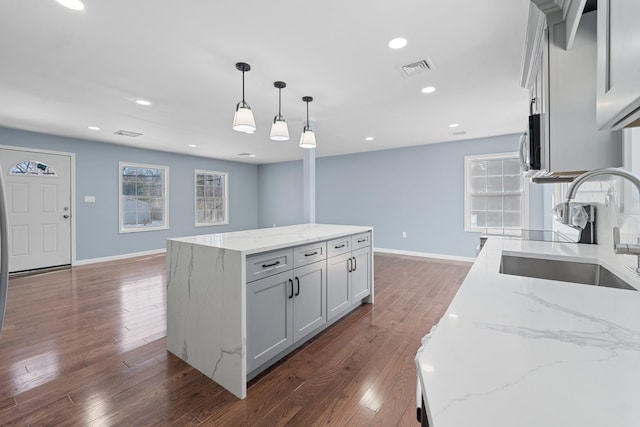 kitchen featuring decorative light fixtures, sink, light stone countertops, dark wood-type flooring, and a spacious island