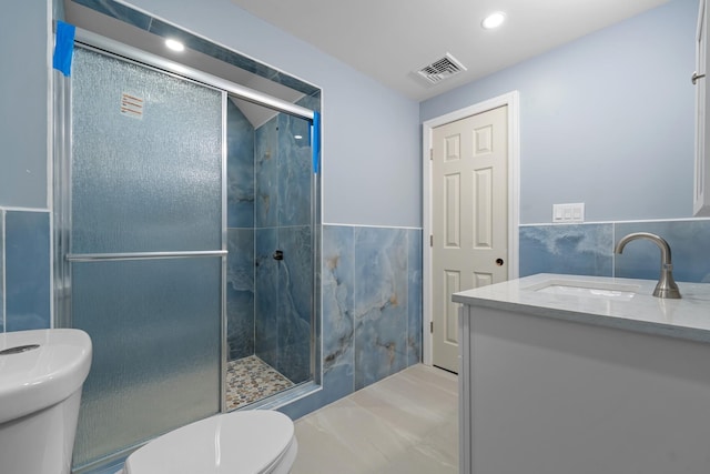 bathroom with walk in shower, vanity, toilet, and tile walls