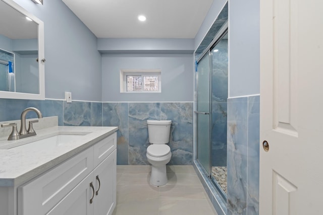 bathroom featuring vanity, toilet, a shower with door, and tile walls