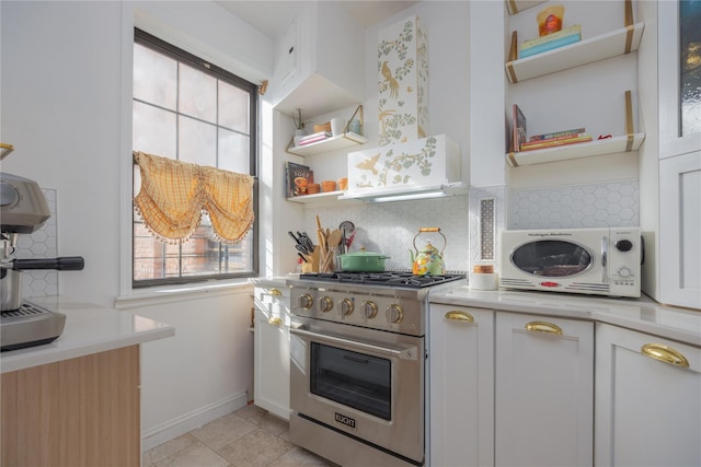 kitchen with decorative backsplash, light tile patterned floors, white cabinets, and high end stove