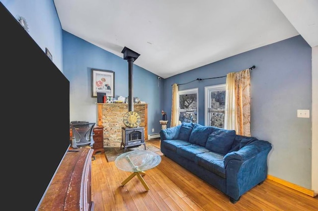 living room with hardwood / wood-style flooring, vaulted ceiling, a baseboard radiator, and a wood stove