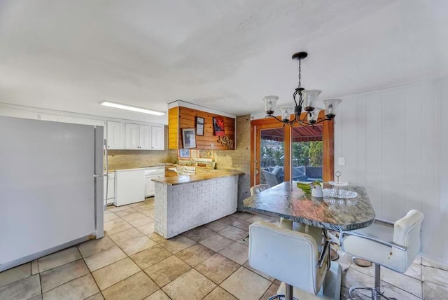 kitchen featuring decorative light fixtures, a chandelier, kitchen peninsula, white appliances, and white cabinets