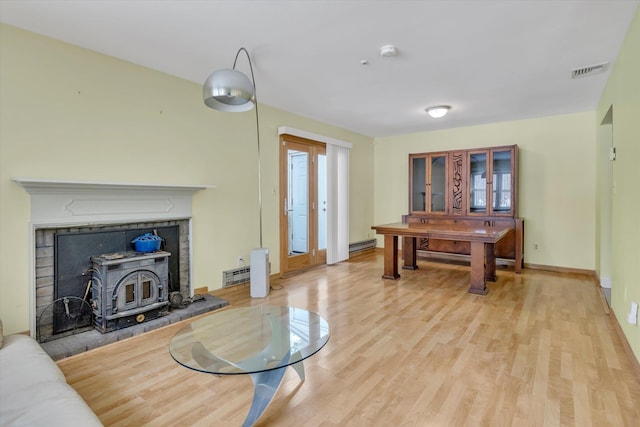 living room featuring a baseboard radiator, a wood stove, and light hardwood / wood-style floors