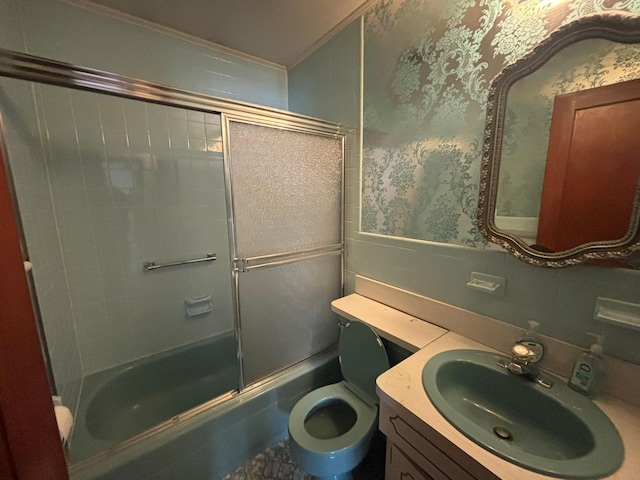 full bathroom featuring toilet, shower / bath combination with glass door, tile walls, ornamental molding, and vanity