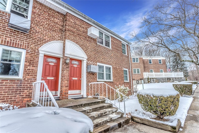 snow covered property entrance with an AC wall unit