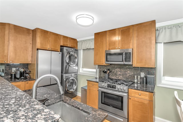 kitchen with stacked washer / drying machine, tasteful backsplash, sink, appliances with stainless steel finishes, and dark stone counters