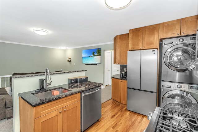 kitchen featuring stacked washer and clothes dryer, stainless steel appliances, dark stone counters, ornamental molding, and sink