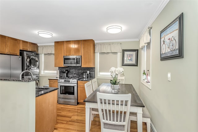 kitchen with stacked washer / drying machine, tasteful backsplash, crown molding, light wood-type flooring, and stainless steel appliances