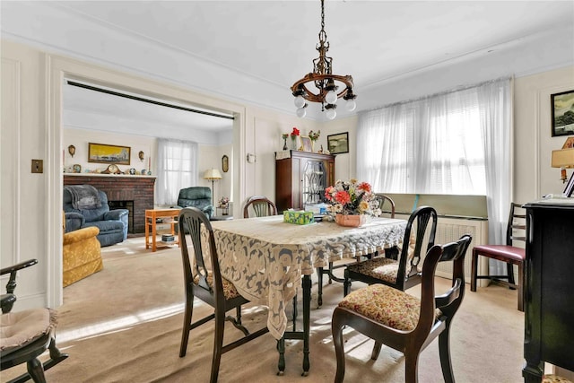 dining area with light carpet, plenty of natural light, a chandelier, and a brick fireplace