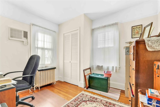 office with light hardwood / wood-style floors, an AC wall unit, and radiator heating unit