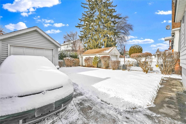 yard layered in snow featuring a garage and an outbuilding