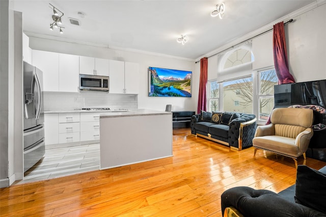 kitchen with appliances with stainless steel finishes, tasteful backsplash, white cabinets, crown molding, and light wood-type flooring