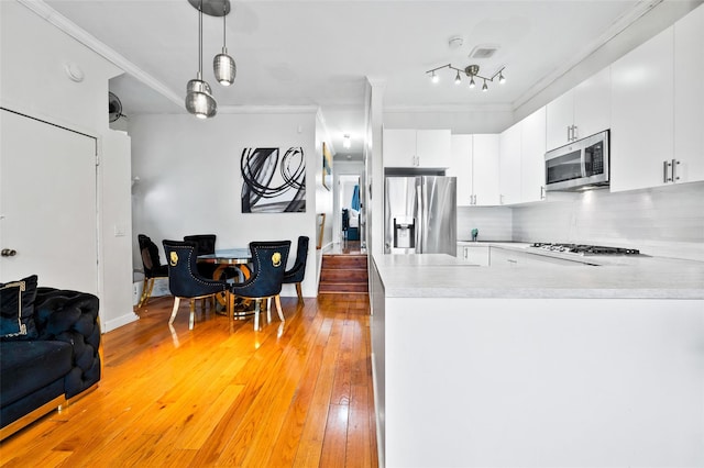 kitchen with appliances with stainless steel finishes, pendant lighting, white cabinetry, decorative backsplash, and light hardwood / wood-style floors