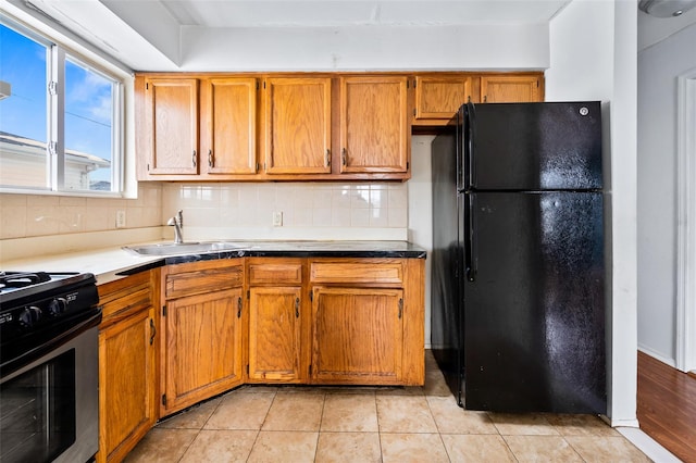 kitchen featuring stainless steel stove, sink, backsplash, light tile patterned floors, and black fridge