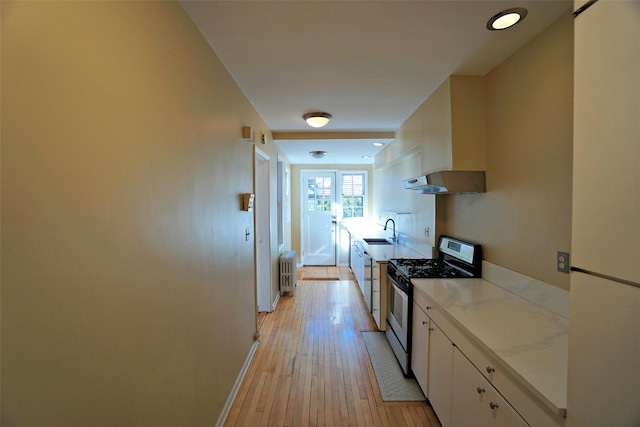 kitchen featuring white cabinets, radiator heating unit, light hardwood / wood-style floors, sink, and stainless steel range with gas cooktop