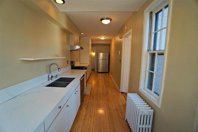 kitchen featuring sink, light wood-type flooring, white cabinetry, radiator, and stainless steel appliances