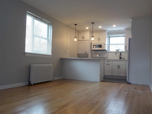 kitchen with white appliances, stacked washer / dryer, radiator, decorative light fixtures, and white cabinetry