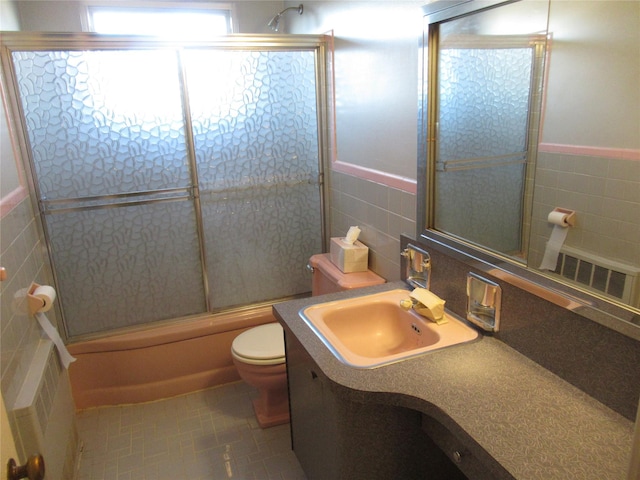 full bathroom with bath / shower combo with glass door, tile walls, vanity, and toilet