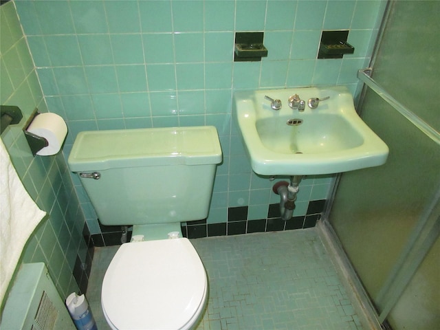 bathroom with a shower with shower door, sink, tile walls, and toilet