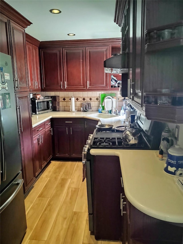 kitchen with tasteful backsplash, gas stove, fridge, sink, and light wood-type flooring