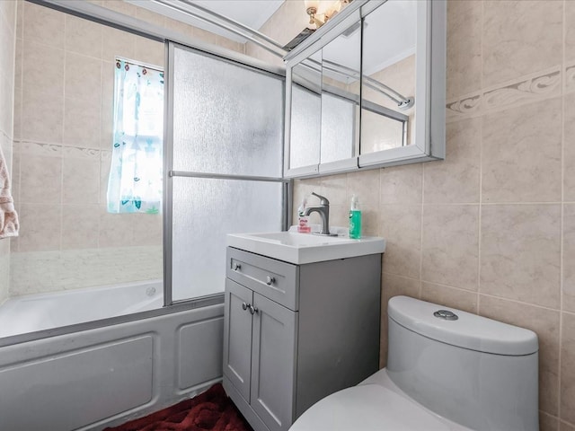 full bathroom with tile walls, shower / bath combination with glass door, vanity, and toilet