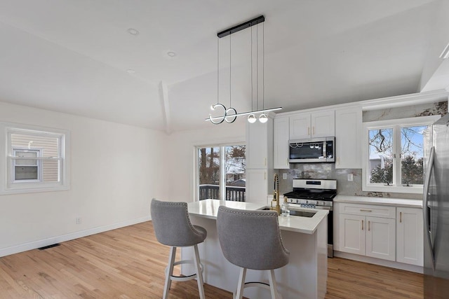 kitchen featuring vaulted ceiling, appliances with stainless steel finishes, pendant lighting, light hardwood / wood-style floors, and white cabinets