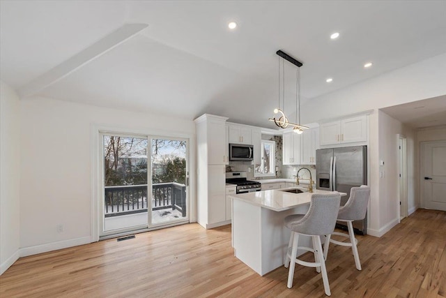 kitchen with decorative light fixtures, stainless steel appliances, a kitchen breakfast bar, and white cabinets