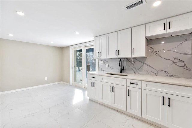 kitchen with tasteful backsplash, sink, light stone counters, and white cabinets