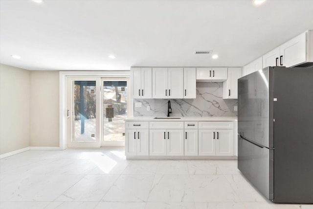 kitchen with tasteful backsplash, sink, white cabinets, and stainless steel refrigerator