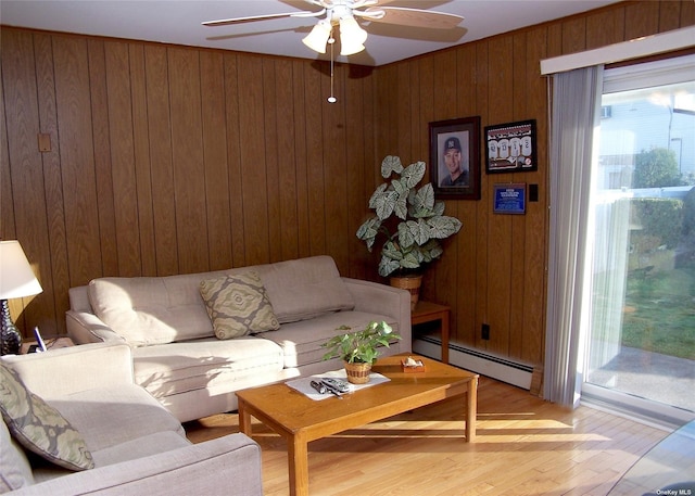 living room with a baseboard heating unit, ceiling fan, light hardwood / wood-style flooring, and wooden walls